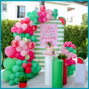 Watermelon birthday party decor in Dubai with green and pink balloon garland, themed cutouts, custom backdrop, and display tables